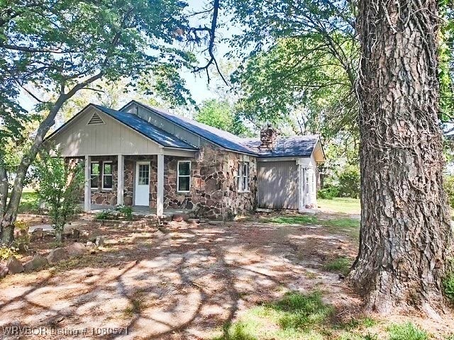 view of front facade with stone siding, covered porch, and a chimney