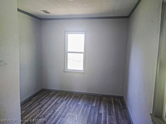 empty room featuring dark wood finished floors, visible vents, ornamental molding, and a textured ceiling