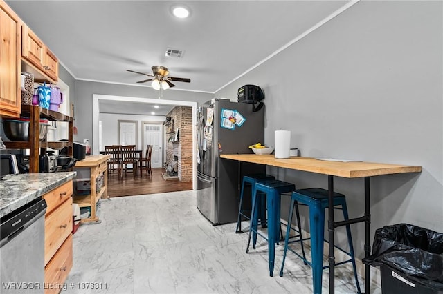 kitchen featuring ornamental molding, a breakfast bar, stainless steel appliances, ceiling fan, and light brown cabinets