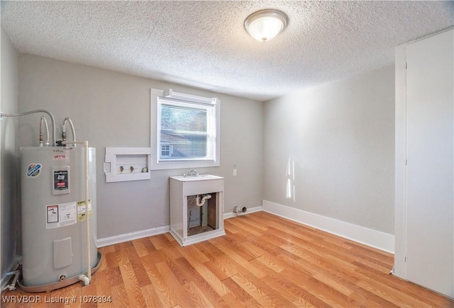 laundry room featuring light wood-type flooring, hookup for a washing machine, electric water heater, and a textured ceiling