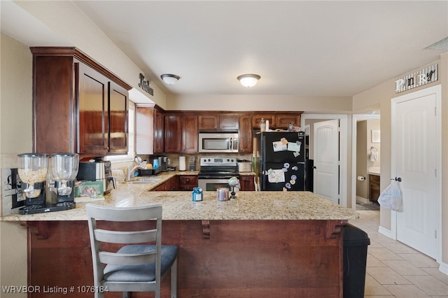 kitchen featuring light stone counters, kitchen peninsula, a kitchen bar, light tile patterned floors, and appliances with stainless steel finishes