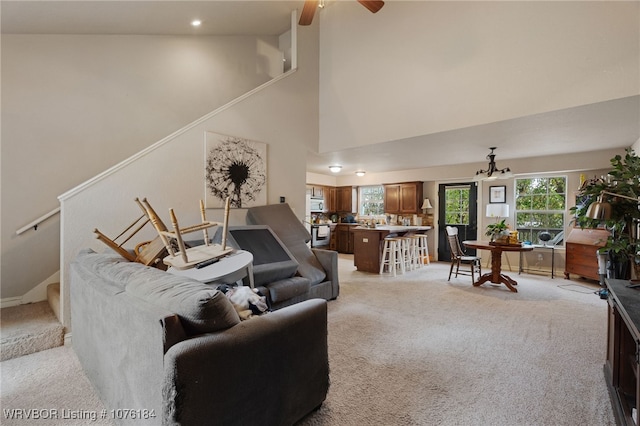 carpeted living room with ceiling fan with notable chandelier and a high ceiling