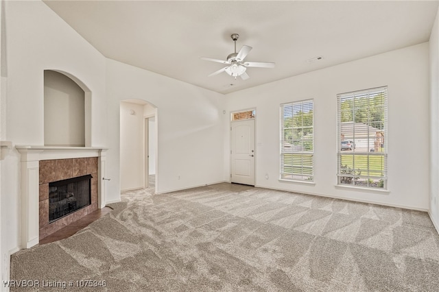 unfurnished living room with a tiled fireplace, ceiling fan, and light colored carpet