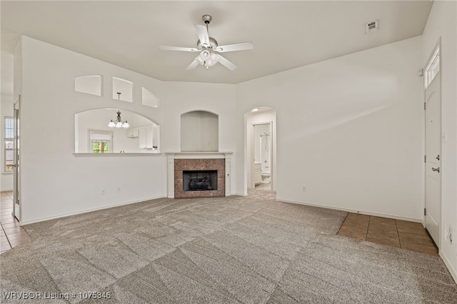 unfurnished living room featuring ceiling fan with notable chandelier, carpet floors, and a tiled fireplace