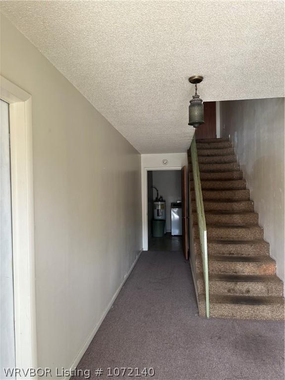 staircase featuring strapped water heater, washer / clothes dryer, carpet, and a textured ceiling