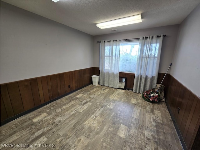 unfurnished room with wooden walls, light hardwood / wood-style floors, and a textured ceiling