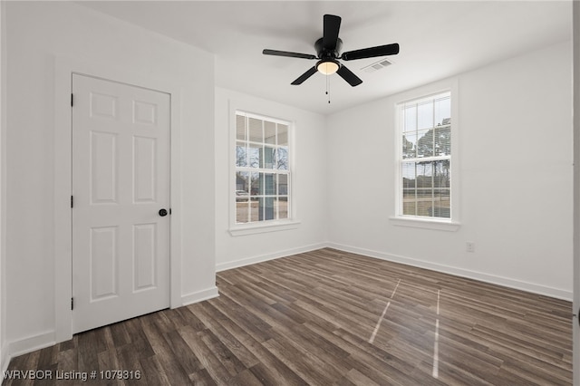 unfurnished room featuring dark wood-style floors, visible vents, baseboards, and a ceiling fan