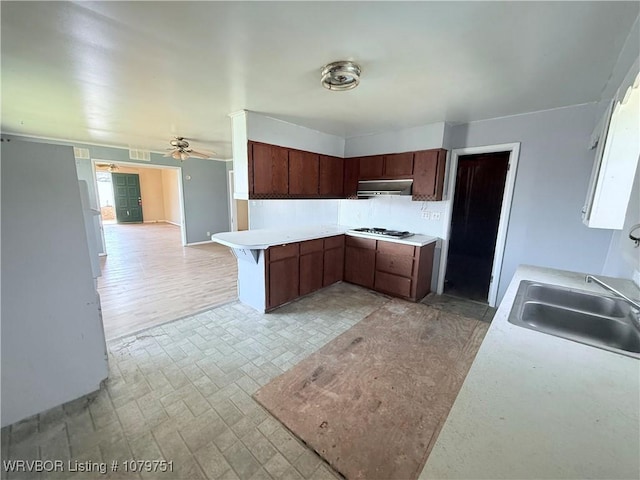 kitchen with range hood, a peninsula, gas stovetop, a sink, and light countertops