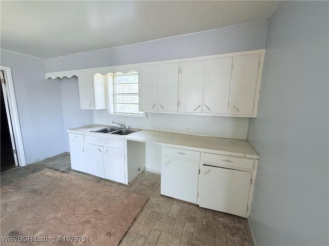 kitchen with a sink, white cabinetry, backsplash, and light countertops