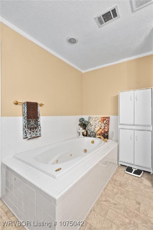 bathroom featuring a textured ceiling, a relaxing tiled tub, and ornamental molding