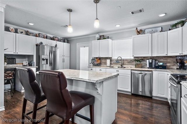 kitchen with appliances with stainless steel finishes, sink, pendant lighting, a center island, and white cabinetry