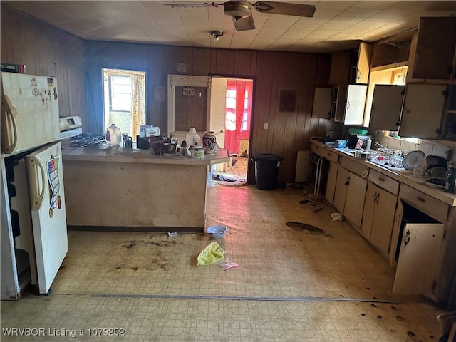 kitchen with a ceiling fan, freestanding refrigerator, wooden walls, and light floors