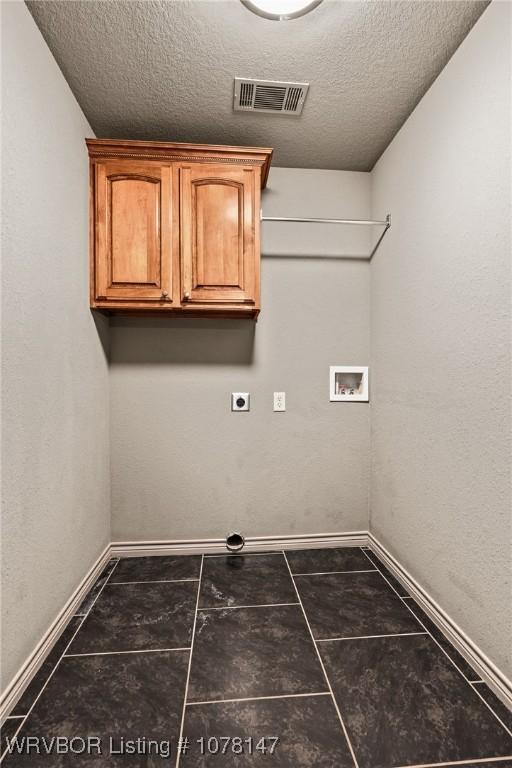 washroom featuring cabinets, electric dryer hookup, dark tile patterned floors, hookup for a washing machine, and a textured ceiling