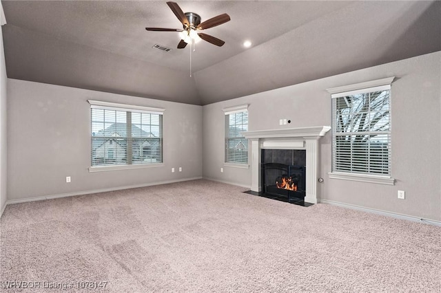 unfurnished living room with a tile fireplace, vaulted ceiling, ceiling fan, a wealth of natural light, and light colored carpet