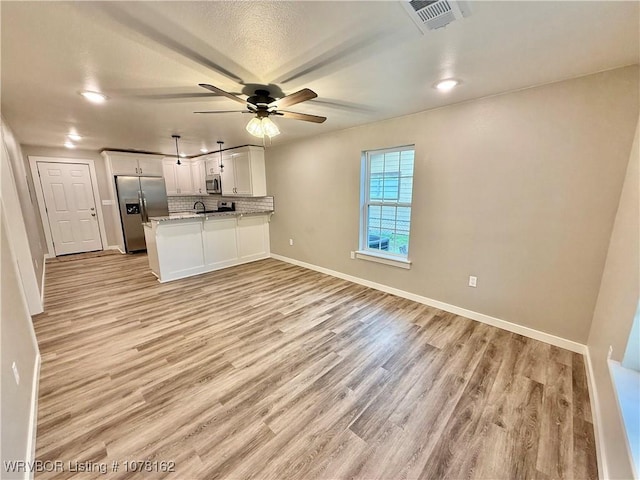 kitchen with white cabinetry, light stone countertops, kitchen peninsula, decorative backsplash, and appliances with stainless steel finishes