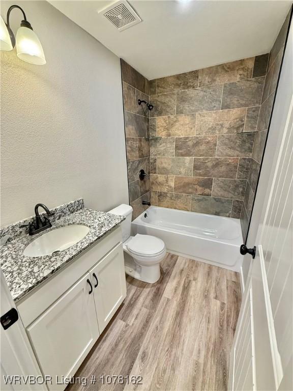 full bathroom with hardwood / wood-style flooring, tiled shower / bath combo, toilet, and vanity