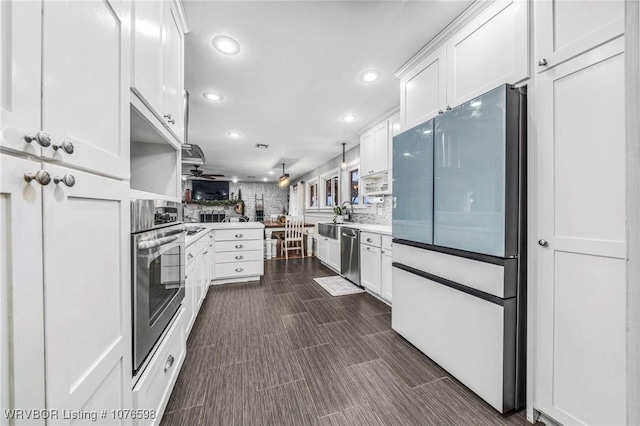 kitchen featuring kitchen peninsula, decorative backsplash, stainless steel appliances, ceiling fan, and white cabinetry