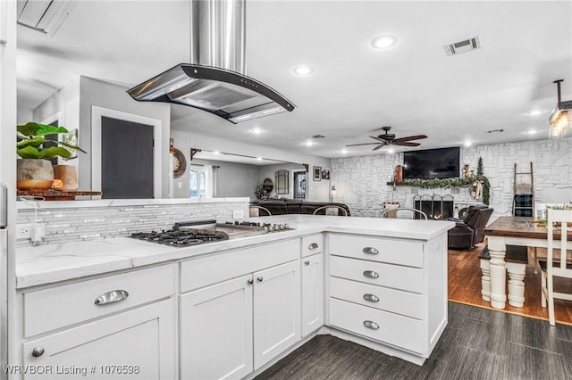 kitchen featuring ceiling fan, kitchen peninsula, stainless steel gas stovetop, island range hood, and white cabinets