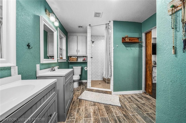 bathroom with a tile shower, vanity, a textured ceiling, and toilet