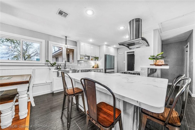 kitchen with white cabinetry, a kitchen breakfast bar, light stone counters, stainless steel fridge, and exhaust hood