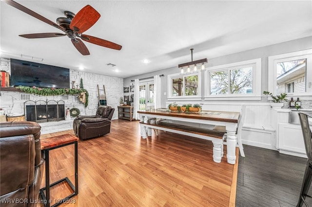 living room with light hardwood / wood-style floors, a stone fireplace, and ceiling fan