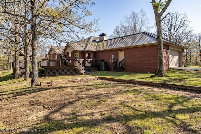 back of house with a chimney, metal roof, central air condition unit, an attached garage, and brick siding