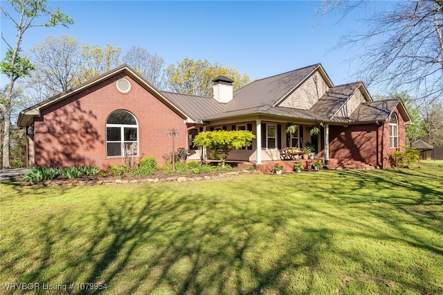 back of house featuring a chimney, a yard, covered porch, brick siding, and a standing seam roof
