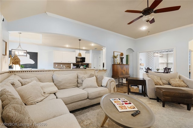 living room featuring vaulted ceiling, ceiling fan with notable chandelier, and ornamental molding