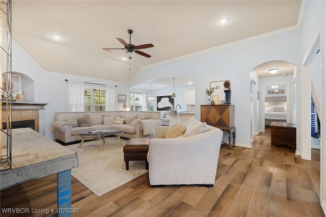 living room featuring light wood-type flooring, vaulted ceiling, ceiling fan, crown molding, and a tile fireplace