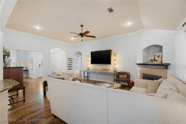 living room featuring a tiled fireplace, ceiling fan, dark wood-type flooring, and ornamental molding