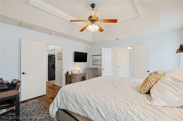 bedroom featuring ceiling fan, wood-type flooring, and a tray ceiling