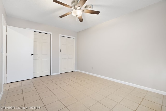 unfurnished bedroom featuring ceiling fan, light tile patterned floors, and multiple closets