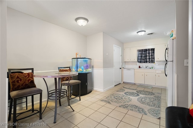 kitchen with sink, light tile patterned flooring, a textured ceiling, white appliances, and white cabinets