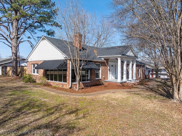 rear view of property with brick siding, a lawn, and a chimney