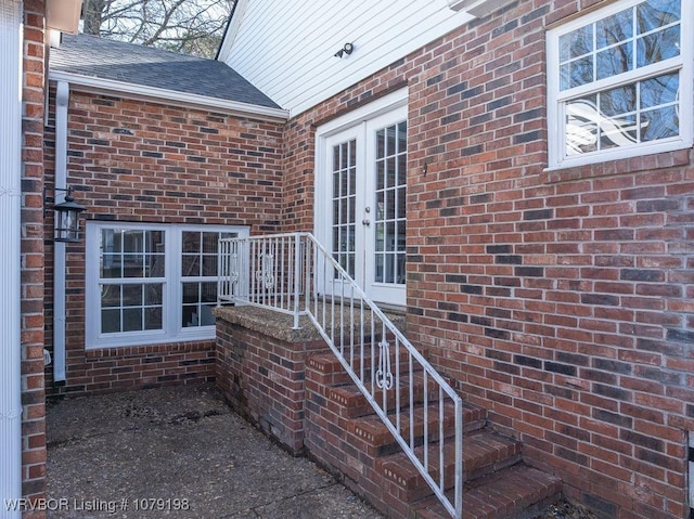 property entrance featuring brick siding, a shingled roof, and french doors