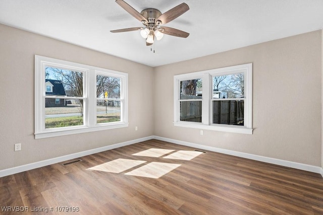 empty room with ceiling fan, wood finished floors, visible vents, and baseboards