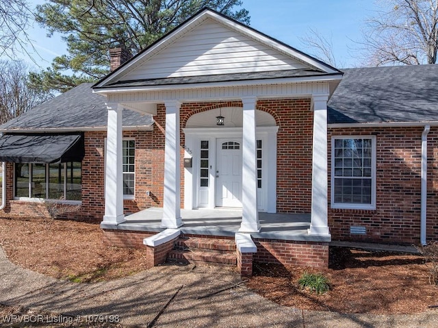 view of front of property featuring a shingled roof, covered porch, and brick siding