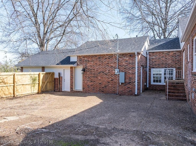 back of property with entry steps, a shingled roof, fence, and brick siding