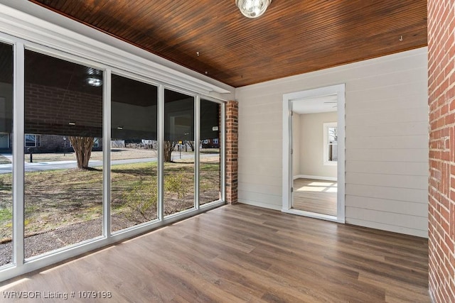 empty room with wooden ceiling, plenty of natural light, brick wall, and wood finished floors