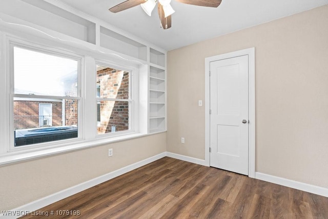 spare room featuring dark wood-style floors, ceiling fan, built in shelves, and baseboards