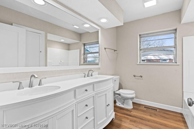 bathroom featuring double vanity, visible vents, a sink, wood finished floors, and baseboards