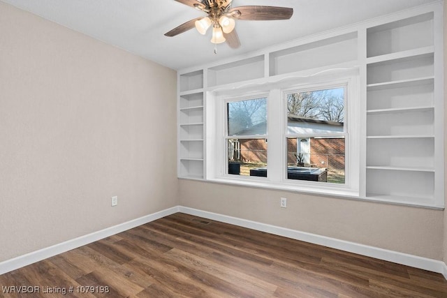 unfurnished room with dark wood-type flooring, built in shelves, baseboards, and a ceiling fan