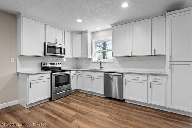 kitchen with appliances with stainless steel finishes, white cabinetry, a sink, and dark wood-style floors