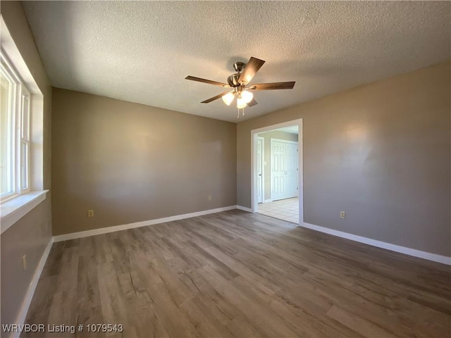 empty room with ceiling fan, baseboards, a textured ceiling, and wood finished floors