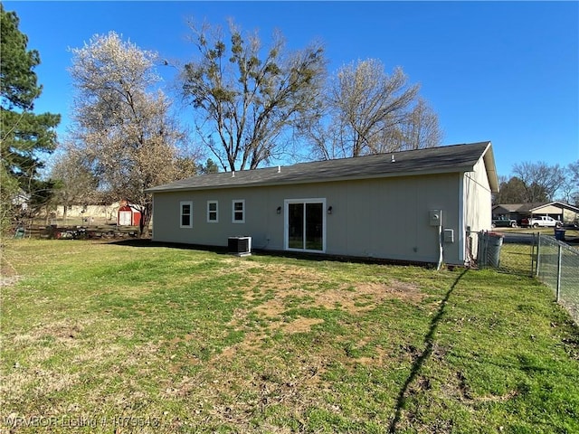 rear view of property with central air condition unit, a lawn, and fence