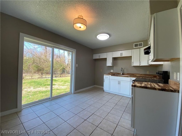 kitchen featuring visible vents, a sink, black range with electric cooktop, light tile patterned flooring, and butcher block counters