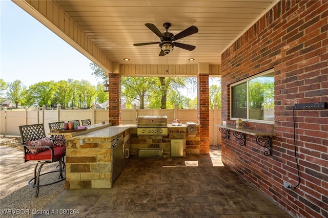 view of patio with an outdoor kitchen, outdoor wet bar, a grill, a fenced backyard, and a ceiling fan