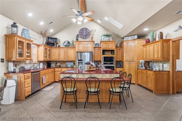 kitchen featuring light tile patterned floors, high vaulted ceiling, an island with sink, and stainless steel appliances
