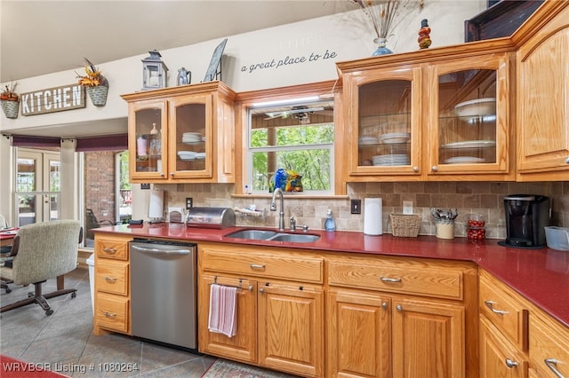kitchen with stainless steel dishwasher, a sink, backsplash, and light tile patterned floors