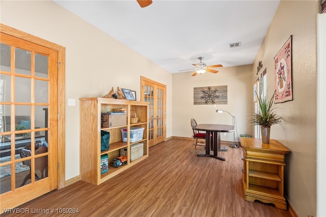 living area with visible vents, baseboards, wood finished floors, and ceiling fan
